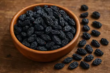 black raisins (currants) placed in a wooden bowl on a table.