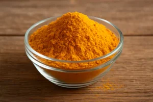 glass bowl filled with bright yellow-orange turmeric powder on a table.