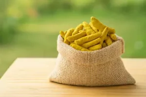 a jute bag filled with whole turmeric sticks placed on a wooden table.