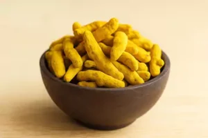 yellow vibrant turmeric sticks in a dark brown wooden bowl.